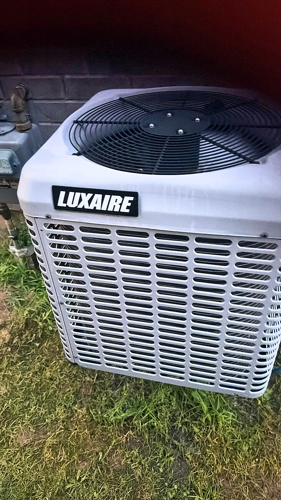 Outdoor air conditioning condenser beside a brick wall, ready for a seasonal check