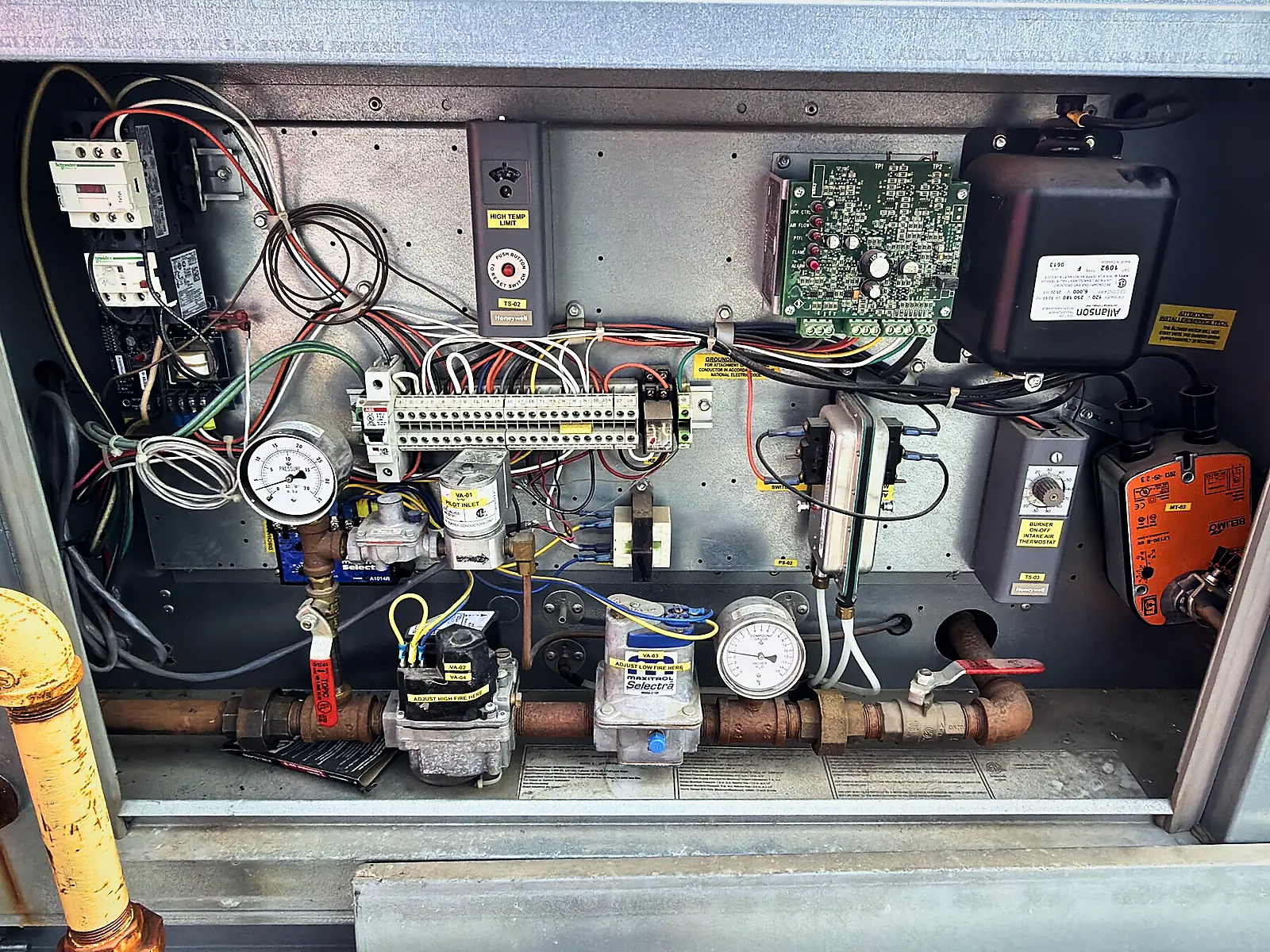 Open control panel of a gas-fired unit showing wiring, gas valve, pressure gauges and controls