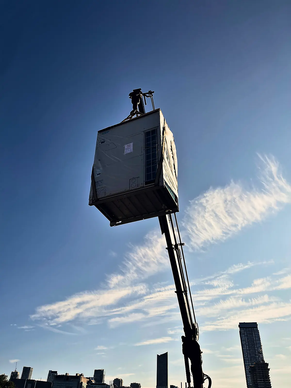Crane lifting a wrapped rooftop unit high above the Toronto skyline
