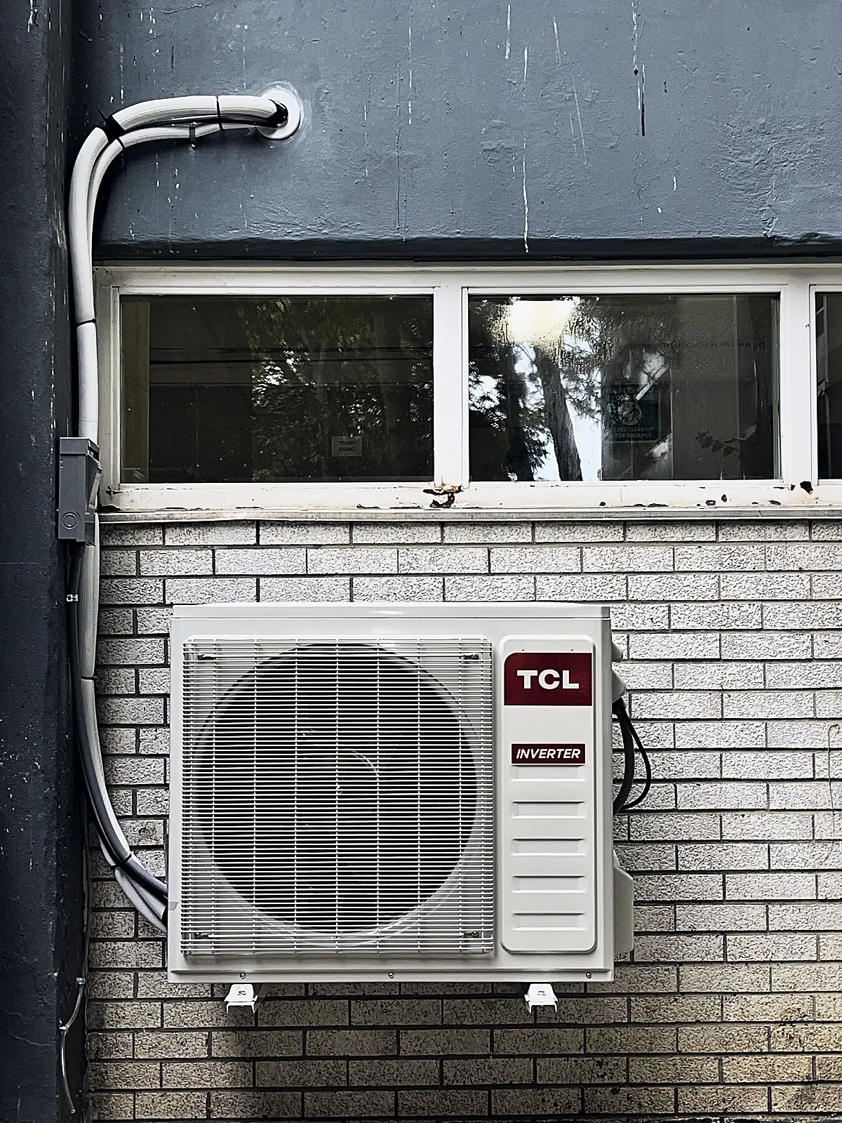 Ductless inverter outdoor unit bracket-mounted on a brick wall below a window