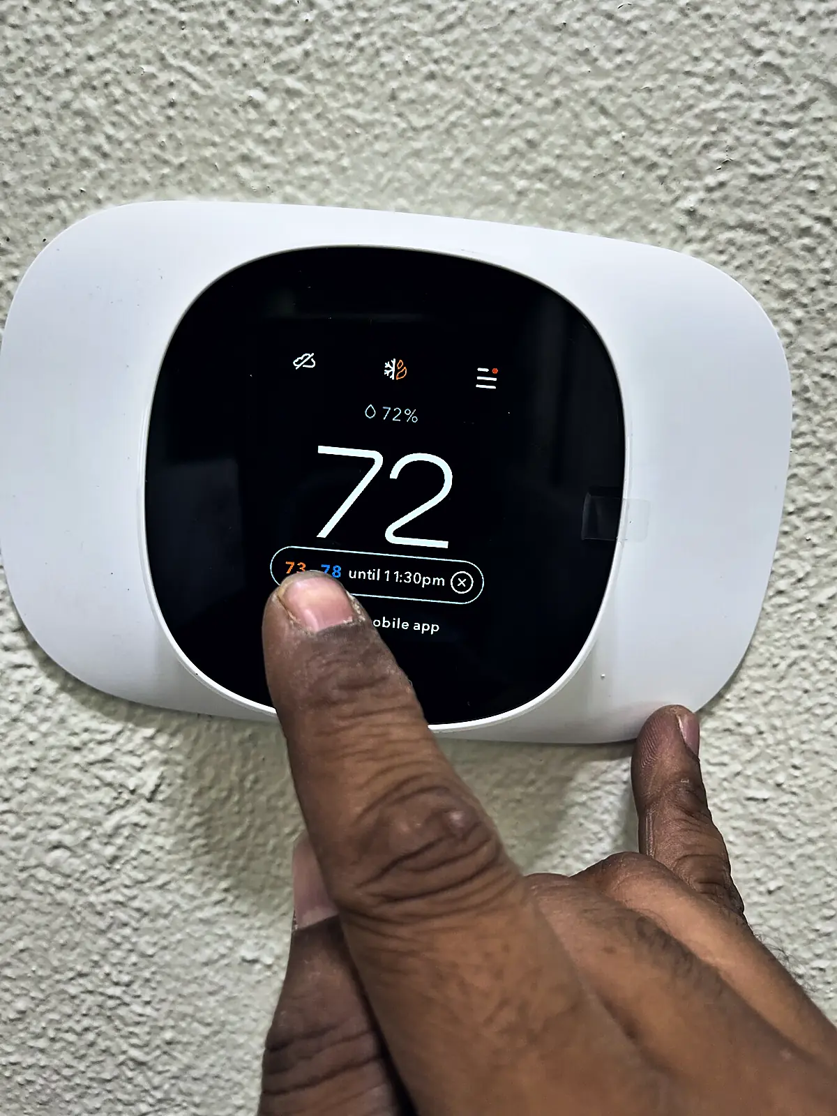 Hand touching the screen of a wall-mounted ecobee smart thermostat