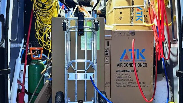 Inside a service van with a boxed air conditioner, a hand truck and tools