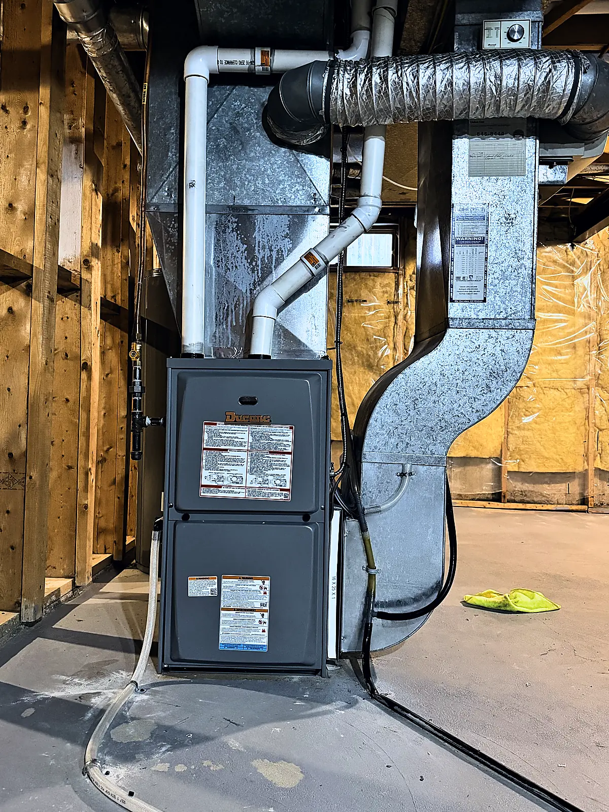 New gas furnace with fresh sheet-metal ductwork and PVC venting in an unfinished basement