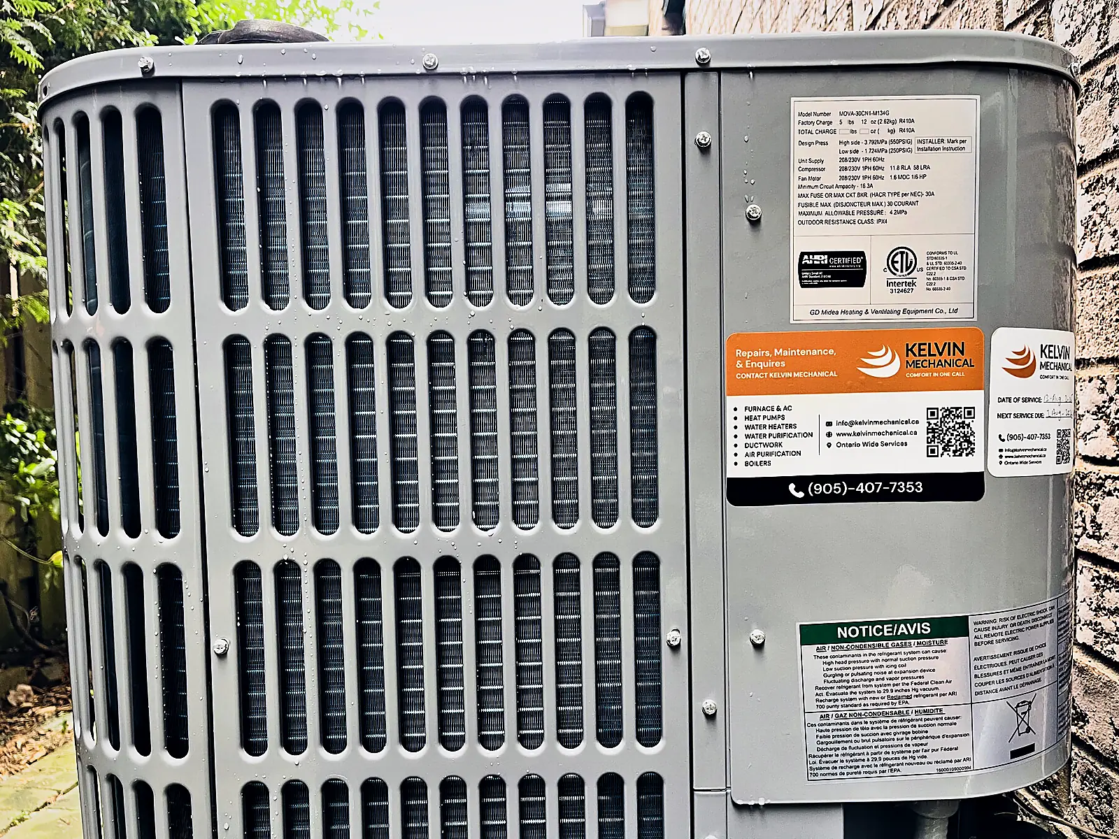 Close-up of an outdoor air conditioner condenser with its rating plate and Kelvin Mechanical service labels