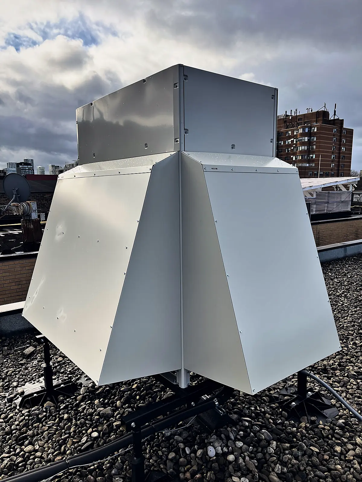 Large white sheet-metal weather hood on a rooftop stand, with city buildings behind