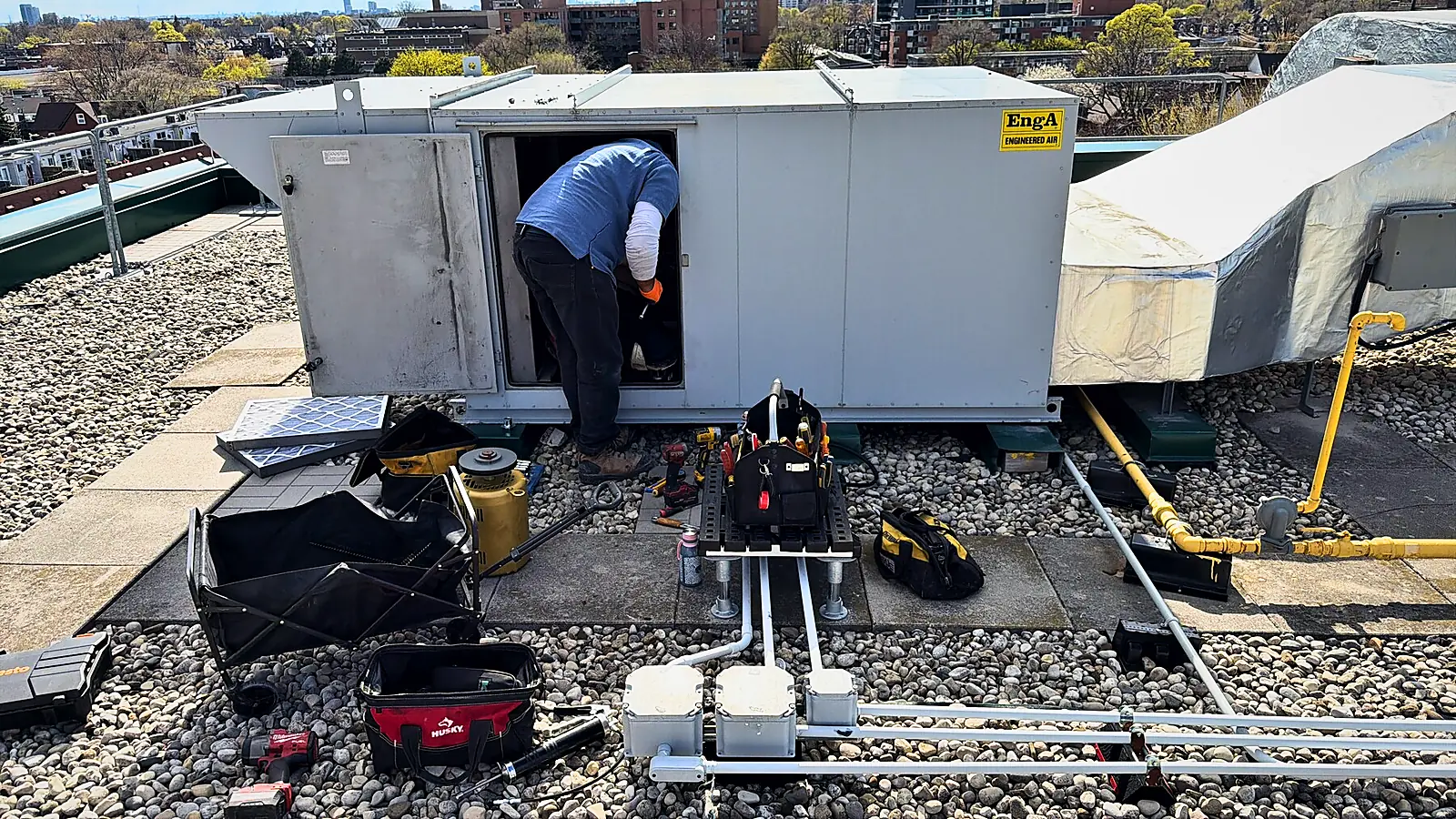 Technician working inside an open rooftop unit on a flat roof with tools laid out