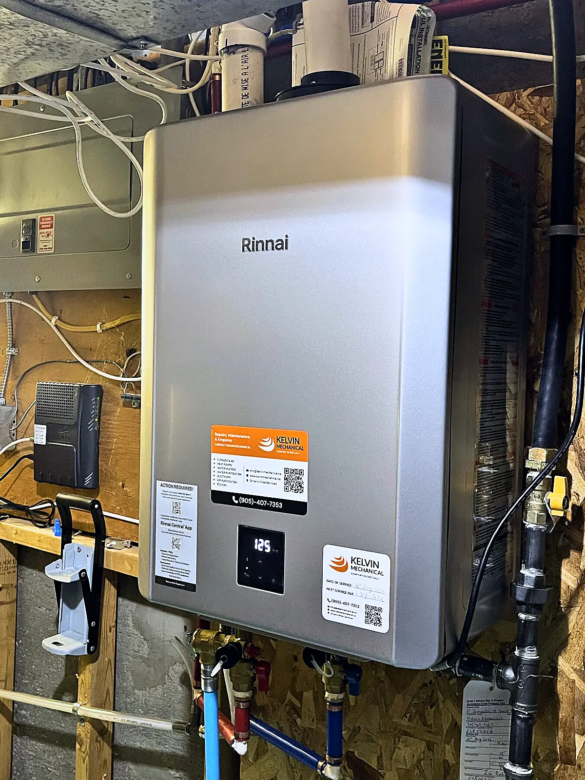 Wall-hung Rinnai tankless water heater with Kelvin Mechanical service labels in a utility room